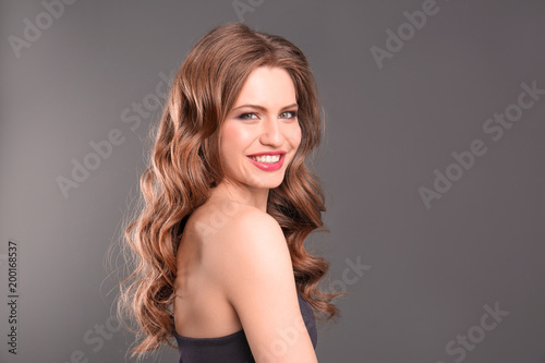 Portrait of young woman with long beautiful hair on grey background