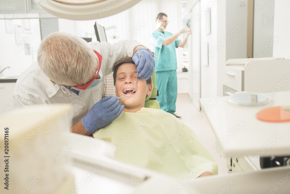 Obraz premium Boy with perfect teeth at the dentist doing check up with the clinic at the background - oral hygiene health care concept