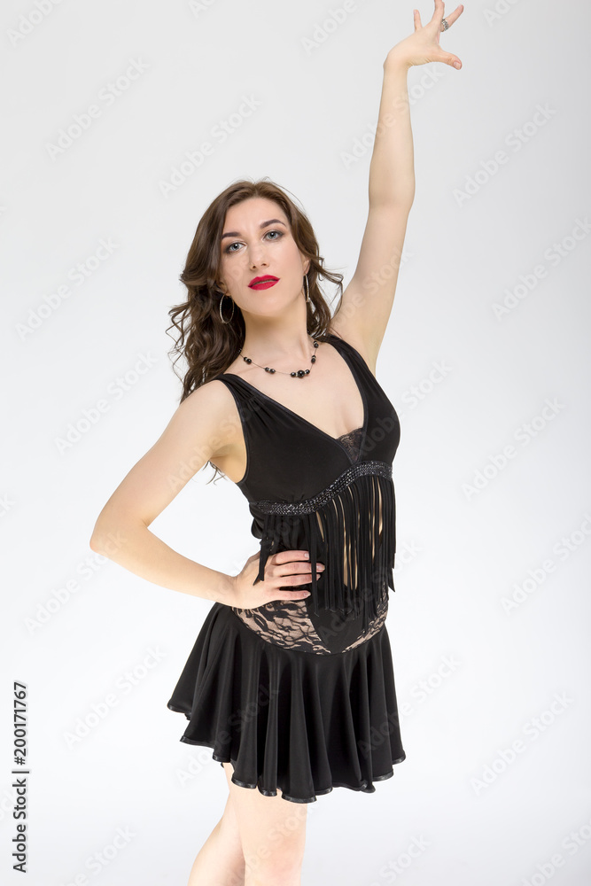 Ballroom dances Ideas and Concepts. Portrait of Female Ballroom Dancer in Black Latin American Dress Against White. Demonstrating New York Position. Ballroom dances Ideas and Concepts. Portrait of Female Ballroom Dancer in Black Latin American Dress Against White. Demonstrating New York Position.