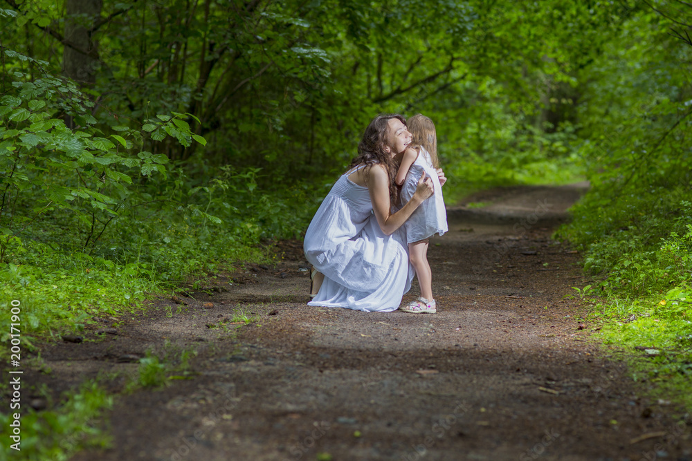 Family Values Concepts. Happy Caucasian Woman with Her Little Child Pembracing in Green Forest. Posing in White Dresses. Family Values Concepts. Happy Caucasian Woman with Her Little Child Pembracing in Green Forest. Posing in White Dresses.
