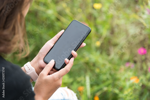 Asian woman wearing smartwatch and using smartphone in her vacation time at green field in selective focus.