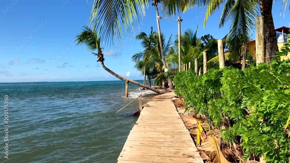 Waves lapping under temporary wooden boardwalk installed as rising seas take the shore of a rustic tourist beach in Bahia, Brazil