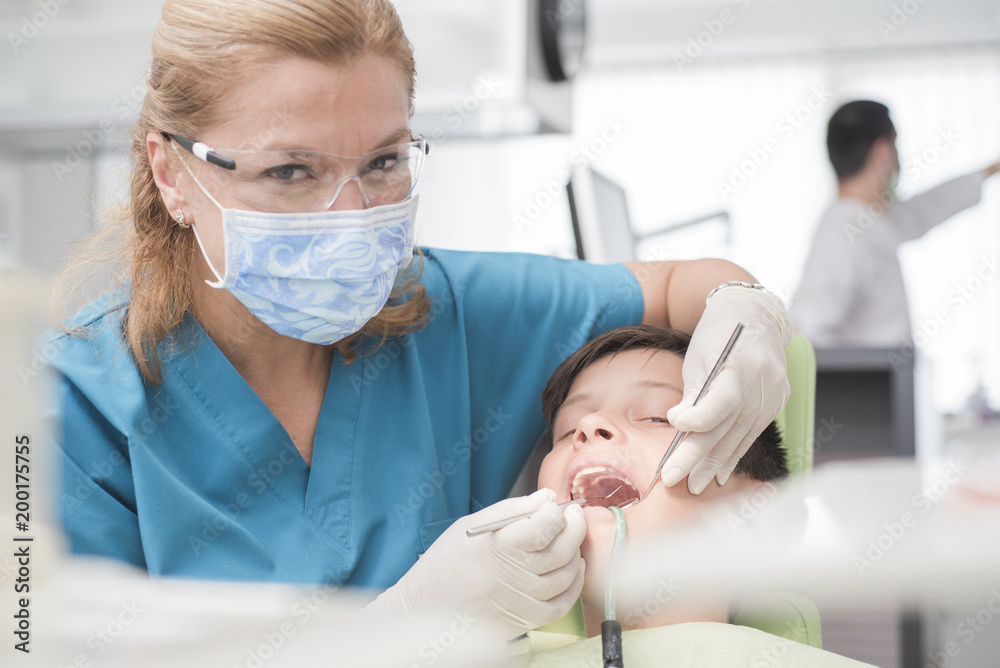 Boy with perfect teeth at the dentist doing check up while other doctors analyze x-ray in the background - oral hygiene health care concept Boy with perfect teeth at the dentist doing check up while other doctors analyze x-ray in the background - oral hygiene health care concept