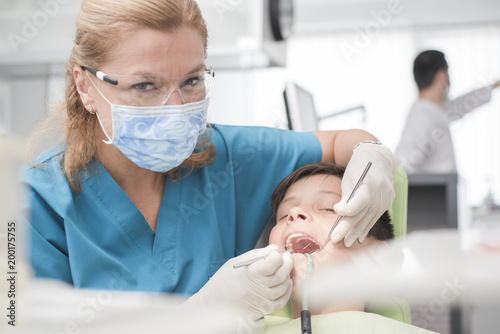 Boy with perfect teeth at the dentist doing check up while other doctors analyze x-ray in the background - oral hygiene health care concept