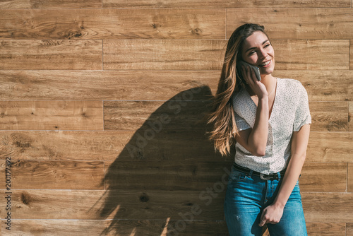 Happy woman using smartphone at a wooden wall