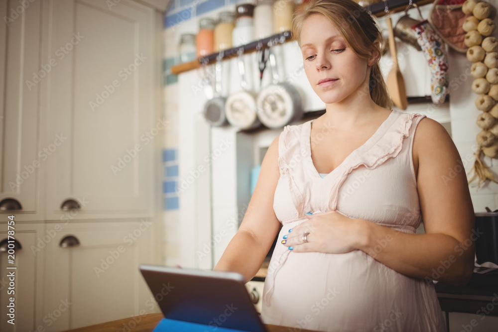 Pregnant woman using digital tablet in kitchen