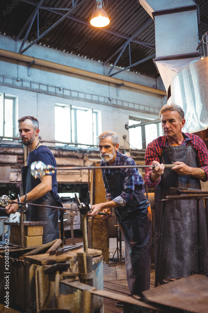Team of glassblowers shaping a glass on the blowpipe Team of glassblowers shaping a glass on the blowpipe