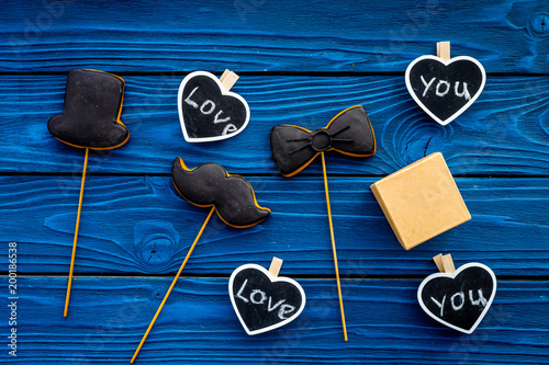 Gift for man on birthday. Gift box among cookies in shape of moustache, hat, bow tie and hearts with lettering love you on blue wooden background top view