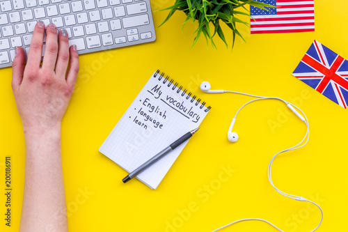 Learn new english vocabulary. Learn landuage concept. Computer keyboard, british and american flags, notebook for writing new vocabulary on yellow background top view photo