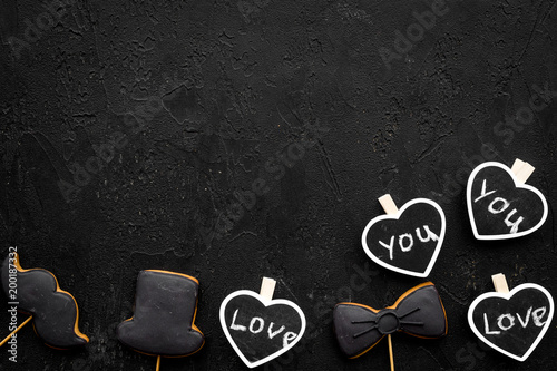 Men's birthday concept. Cookies in shape of moustache, hat, bow tie. Hearts with lettering love you on black background top view copy space