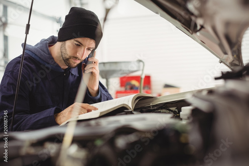 Mechanic reading instruction manual while talking on a mobile phone photo