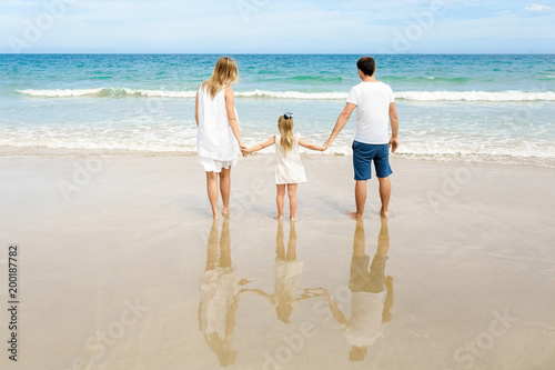 Back view of happy family are standing on the tropical beach.