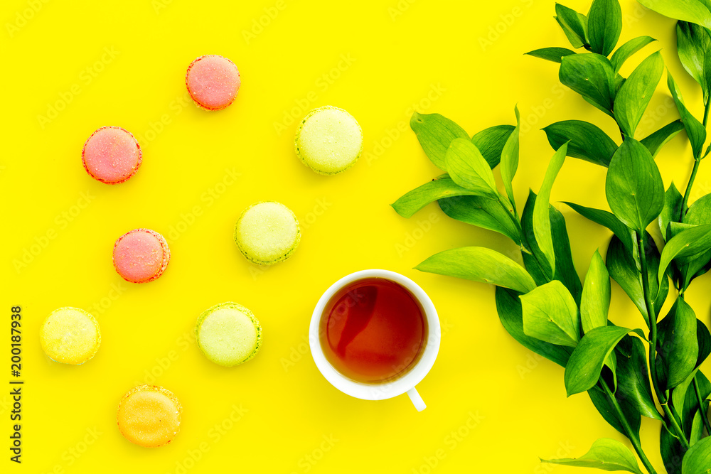 Summer mood, summer tea party. Cup of tea and sweets macarons near brignt greenery on yellow background top view
