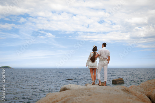 Back view of young couple standing on rocks by the sea. Copy space.