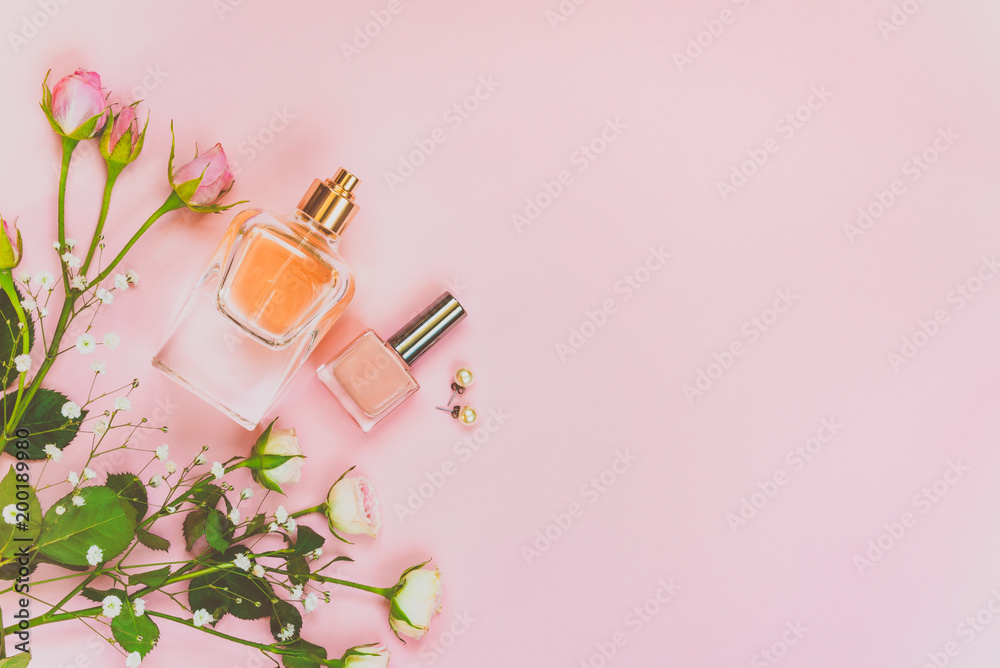 Flat lay of female cosmetics products and accessories. A bottle of perfume, nude nail polish, pearl earings and roses over pink background. Copy space. - obrazy, fototapety, plakaty 
