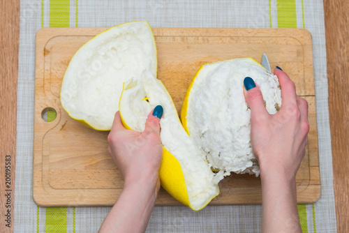 Girl cleans a pomelo on a wooden board photo