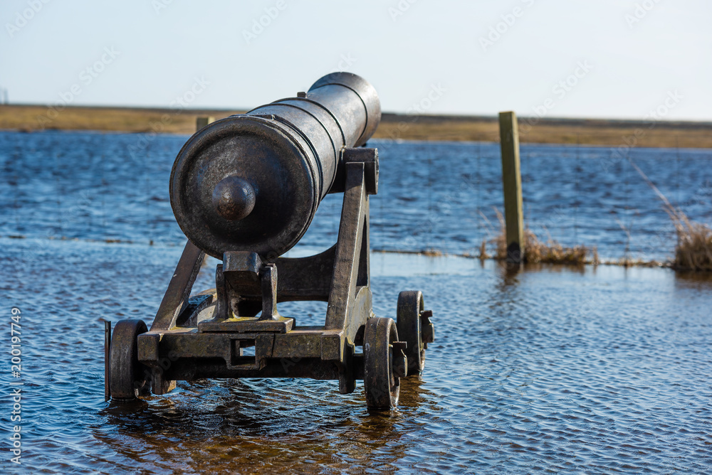 Cast iron ship cannon on flooded coastal area. Logo removed.