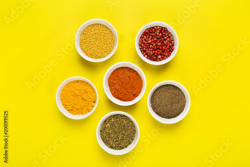 Various spices in bowls on yellow background. Top view. Food background