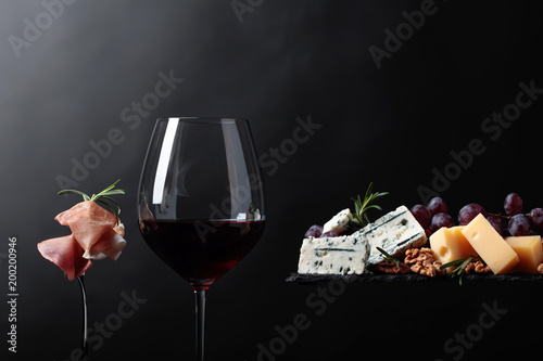 Glass of red wine with various cheeses , grapes and prosciutto .