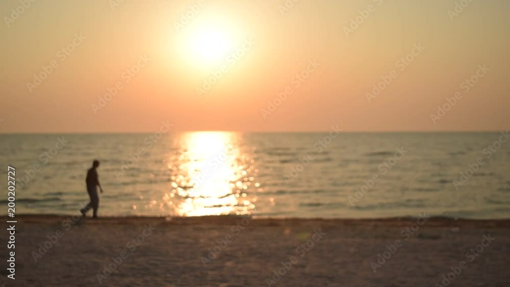 Unidentifiable man walks along shore on beach at dawn during sunrise in the morning. Defocused video. Unidentifiable man walks along shore on beach at dawn during sunrise in the morning. Defocused video.