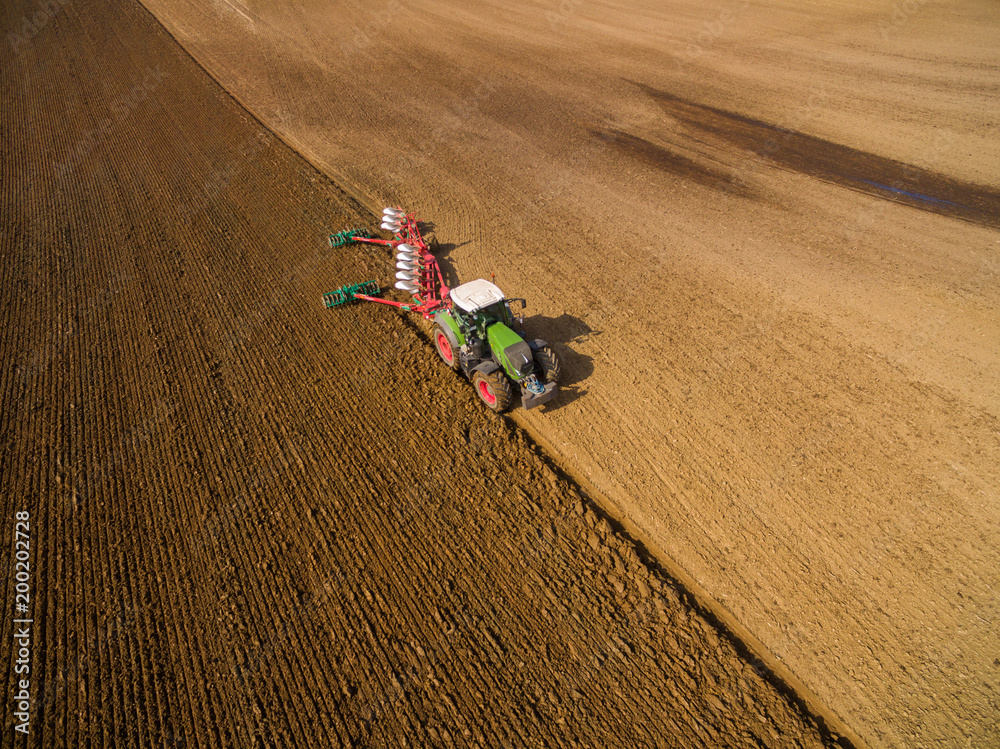 Tractor plowing a agricultural field - aerial view - Tractor cultivating arable land for seeding crops