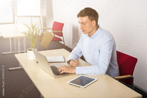 Young businessman using his laptop, indoors office. © Wisiel
