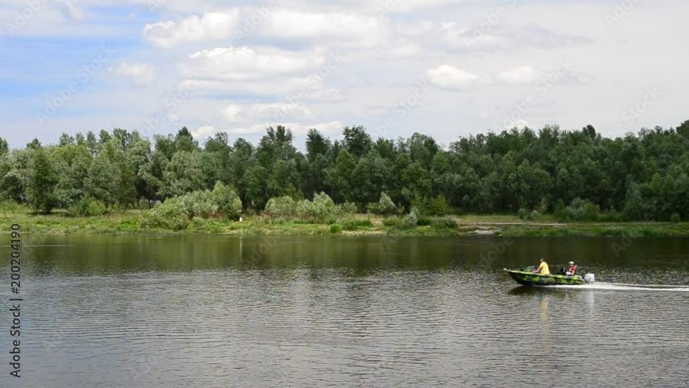 Motor boat moving fast on water surface of Desna river near Kiev, Ukraine, in summer on background of lush green foliage on river bank Motor boat moving fast on water surface of Desna river near Kiev, Ukraine, in summer on background of lush green foliage on river bank