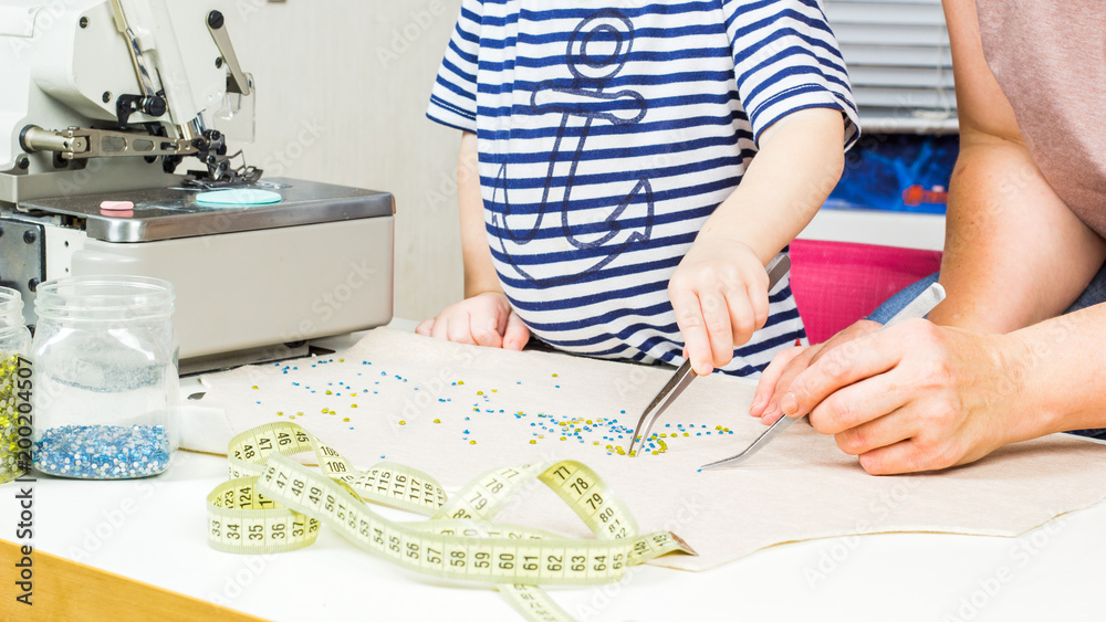 Mother and child make a pattern of beads on the fabric. Mother and child make a pattern of beads on the fabric.
