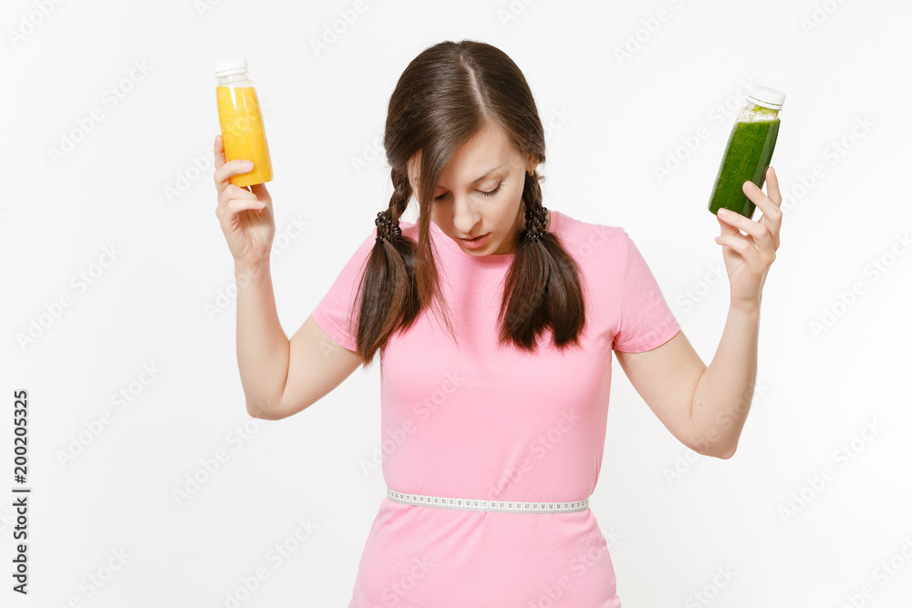 Woman holds green, yellow detox smoothies in bottles, measure tape on waist isolated on white background. Proper nutrition, vegetarian drink, healthy lifestyle, dieting concept. Copy space, flack. Woman holds green, yellow detox smoothies in bottles, measure tape on waist isolated on white background. Proper nutrition, vegetarian drink, healthy lifestyle, dieting concept. Copy space, flack.