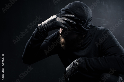  Burglar in balaclava leaning his head on hand