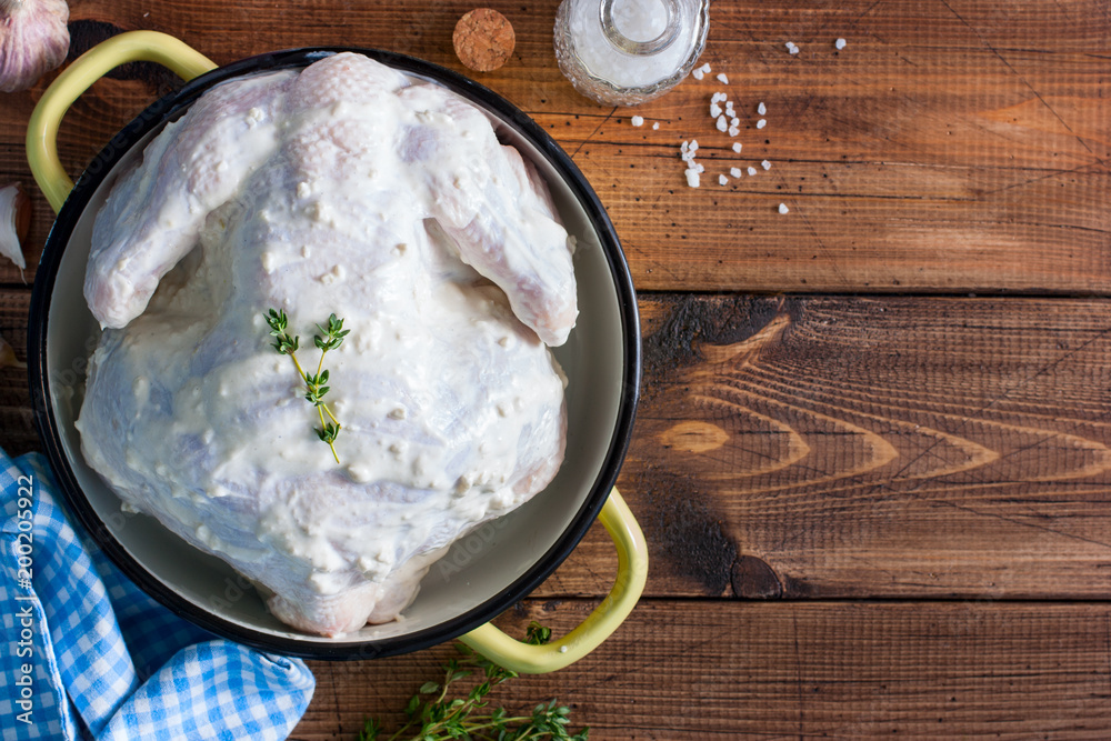 Raw whole chicken marinated with garlic, thyme, spices for baking in the oven or on the grill, top view, copy space Raw whole chicken marinated with garlic, thyme, spices for baking in the oven or on the grill, top view, copy space