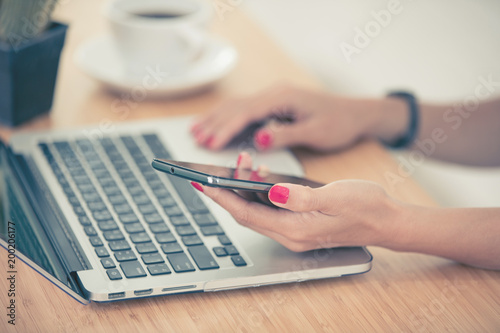 Close up woman hands using smartphone and laptop
