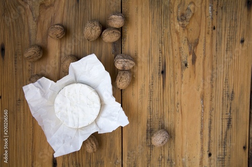 Round cheese camembert or brie in paper on wooden background with walnuts . Copy text.