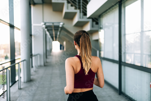 Young sports woman runner running indoors. Rear view.