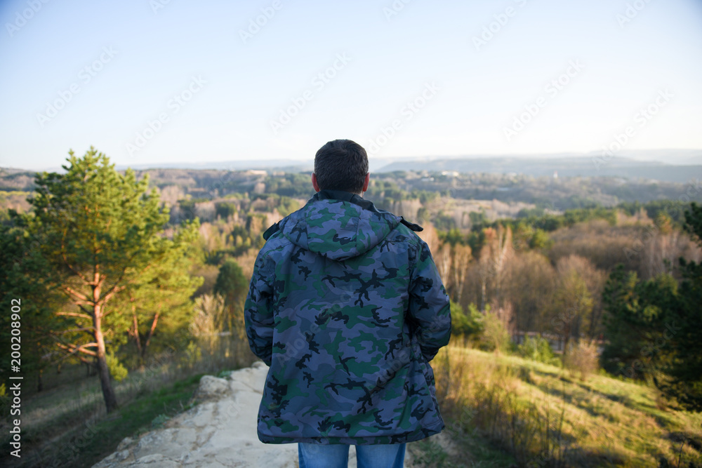 adult man in sport jacket looks at beautiful forest mountains landscape scenery in spring