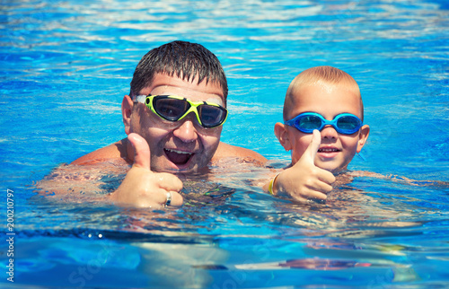 Father and son jump and swim in the pool under sun light at summer day. Leisure and swimming at holidays. © Denis