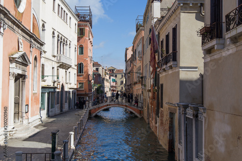 Narrow Venetian street with people on a bridge across water canal