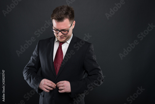 Portrait of business man wearing black suit buttoning jacket.