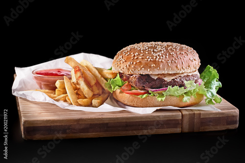 burger with french fries on wooden cutting board isolated on black background photo