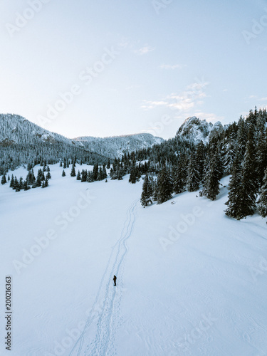 Aerial view of a young hiker caucasian backpacker walking on a icy footpaths. Winter snow covered mountains. 
