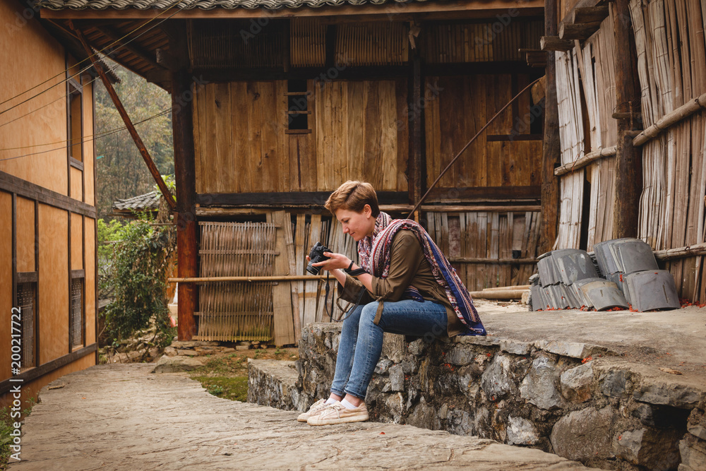 Tourist woman watches her pictures on holiday in a wooden village