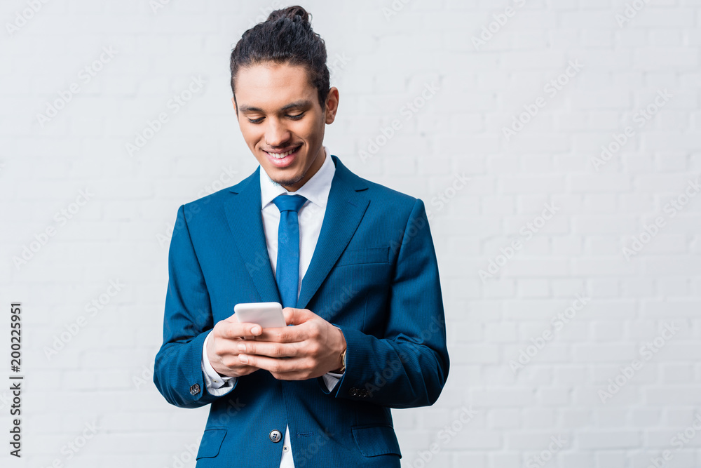 African american businessman using smartphone on white wall background