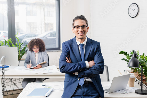Smiling businessman standing in office with his female coworker by table with computer