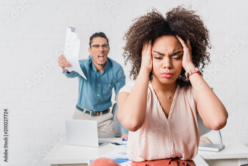 Woman suffering from stress because of angry male colleague in office