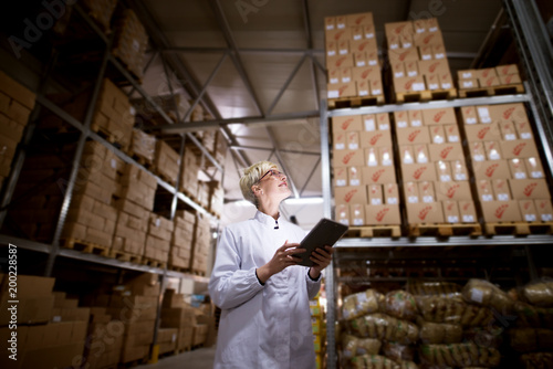 Obraz na płótnie Young cheerful gorgeous worker is using a tablet to check if production quota was achieved in factory cargo area
