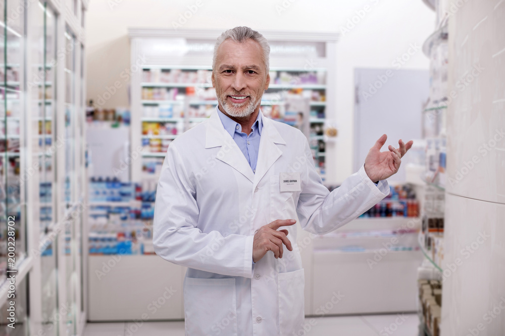 Welcome here. Mature cheerful male pharmacist gesturing while smiling to camera