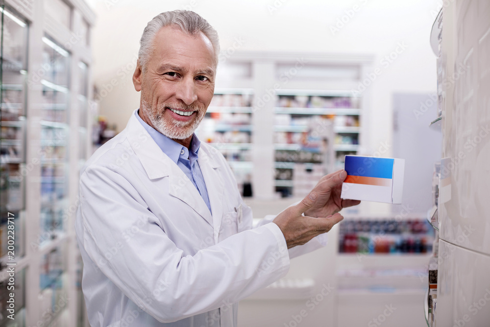 New drug. Senior happy male pharmacist looking at camera while holding drug