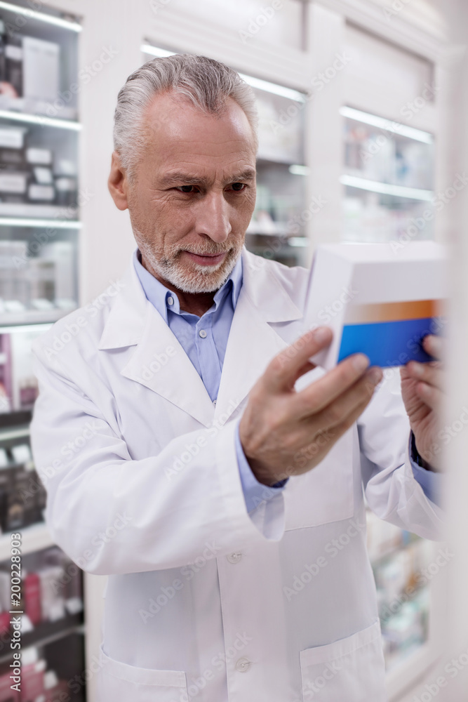Be aware. Mature handsome male pharmacist reading while carrying medication Be aware. Mature handsome male pharmacist reading while carrying medication