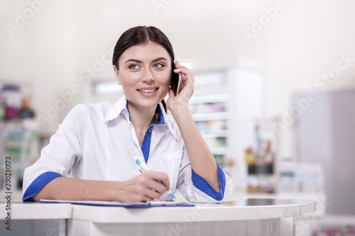 Medicine supply. Inspired female pharmacist calling while taking notes