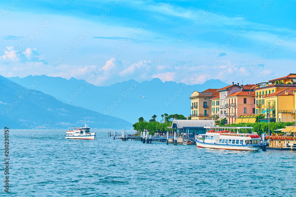Ship arriving to Bellagio town quay at lake Como in Italy with beautiful hotels, blooming nerium oleander flowers and boats